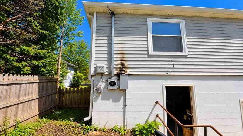 Charred siding above a damaged meter box and service mast on a house exterior